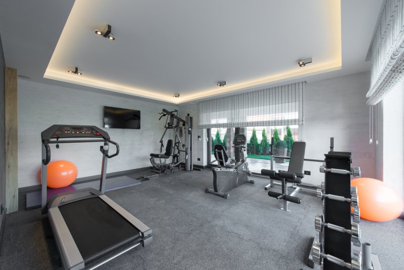 A gray home gym with a lot of workout equipment and rubber floor mats (Photo by poplasen - stock.adobe.com)